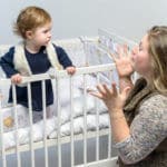 Einschlafprobleme Mutter verzweifelt vor dem Babybett knieend mit nicht schlafen wollenden Baby darin