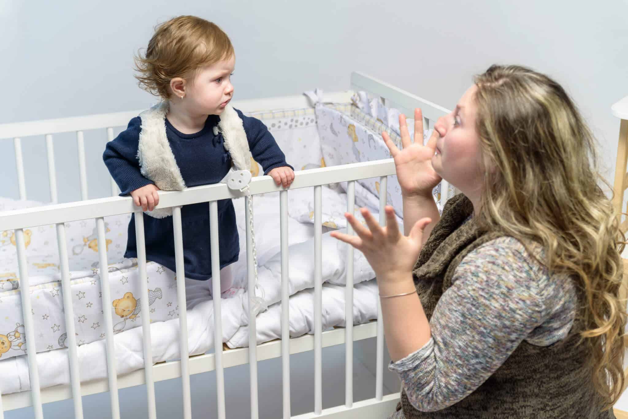 Einschlafprobleme Mutter verzweifelt vor dem Babybett knieend mit nicht schlafen wollenden Baby darin