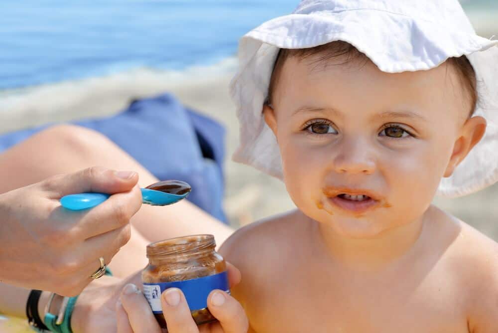 Der erste Urlaub mit dem Baby - Mutter füttert Kleinkind mit einem Brei