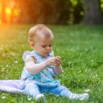 Achtsamkeit Kleinkind sitzt mit Pflanze in der Hand auf einer Wiese