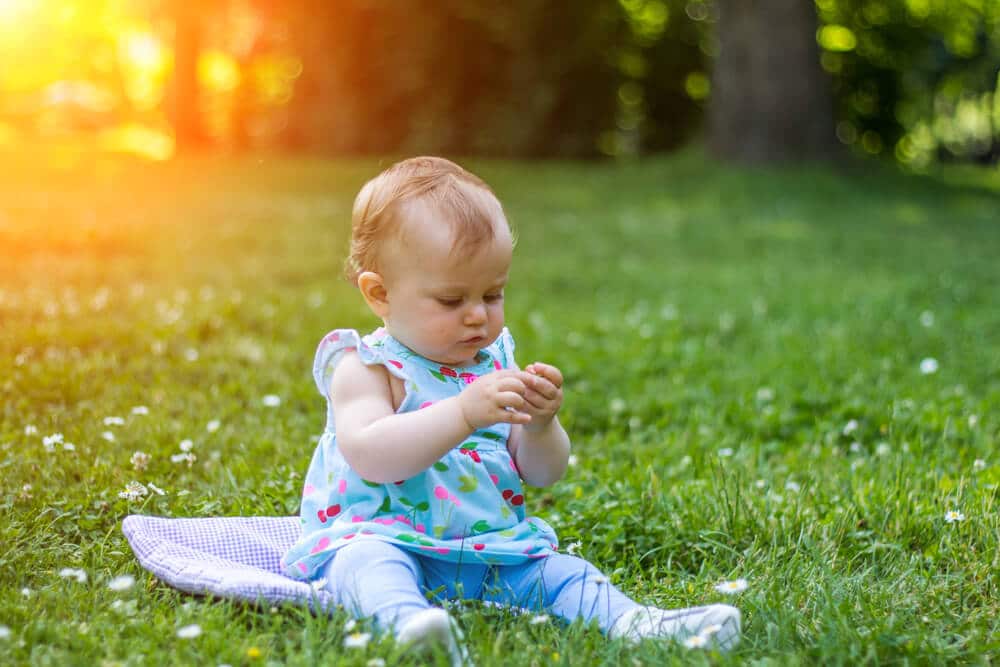Achtsamkeit Kleinkind sitzt mit Pflanze in der Hand auf einer Wiese