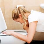 Hyperemesis Schwangere hockt gebückt über einer Kloschüssel