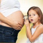 Geschwisterkind: Kind hört mit Glas am Bauch der Mutter