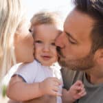 Partnerschaft - Eltern küssen ihr Baby von links und rechts