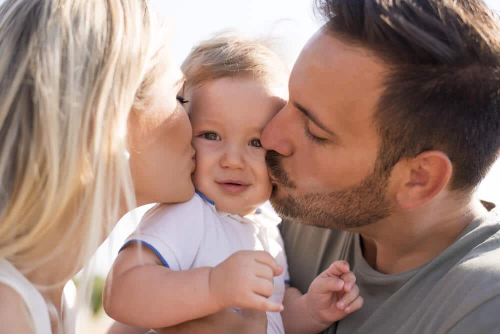 Partnerschaft - Eltern küssen ihr Baby von links und rechts