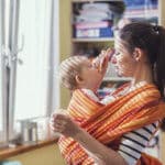 Babys tragen Mutter trägt Kind in einem Tragetuch und füttert es