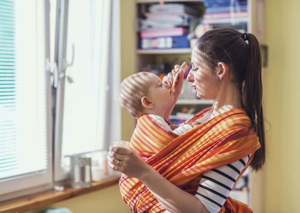 Babys tragen Mutter trägt Kind in einem Tragetuch und füttert es