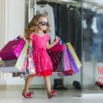 Erziehung ohne Nein - Kleines Mädchen kommt mit Einkaufstaschen bepackt aus einem Laden