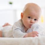 Baby liegt auf dem Bauch und trinkt eine Nuckelflasche