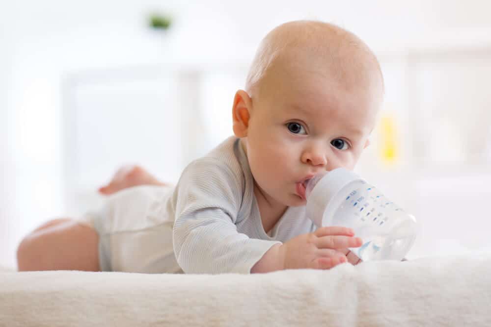 Baby liegt auf dem Bauch und trinkt eine Nuckelflasche