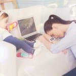 müde Eltern - Mutter sitzt müde vor der Coach mit ihrem Baby und Laptop