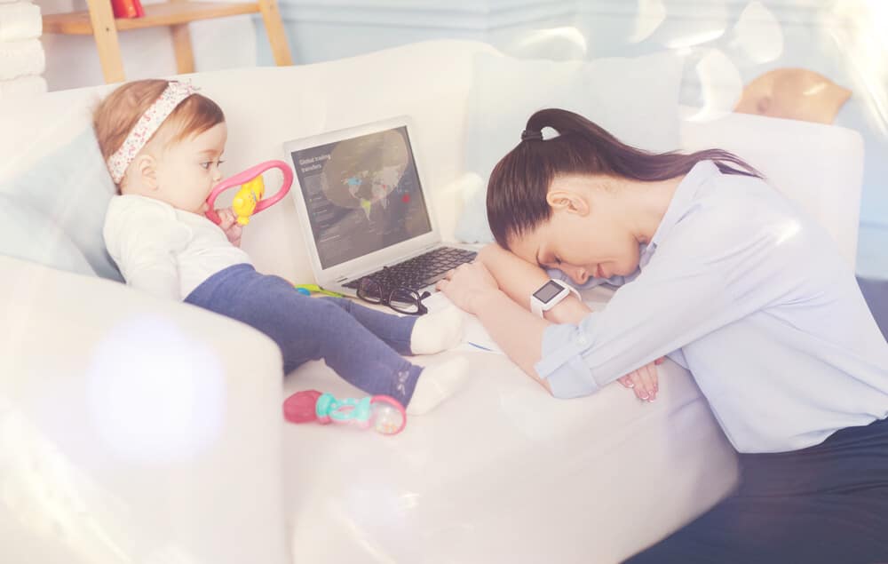 müde Eltern - Mutter sitzt müde vor der Coach mit ihrem Baby und Laptop