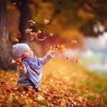 Jahreskreis Herbst - Kind spielt sitzend im Laub